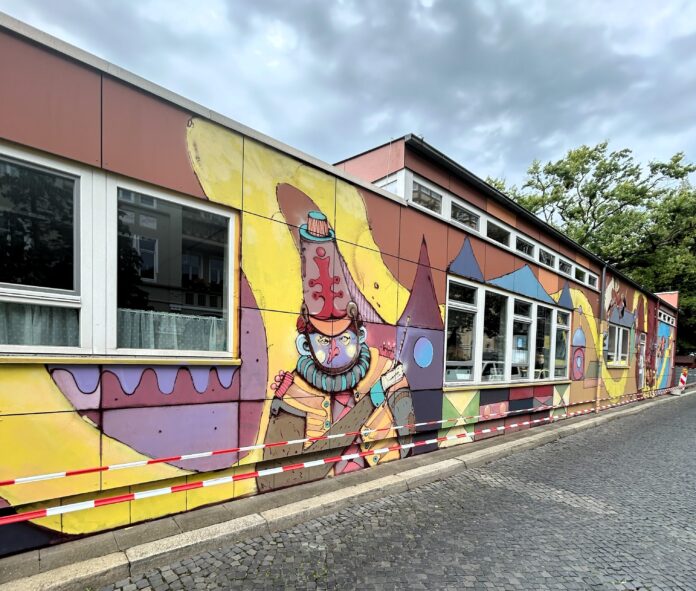 Ein buntes Männchen schaut von der Fassade der Kindertagesstätte Das neue Kunstwerk für die Kindertagesstätte zeigt, wie Street-Art zur Verschönerung von Gebäuden beitragen kann